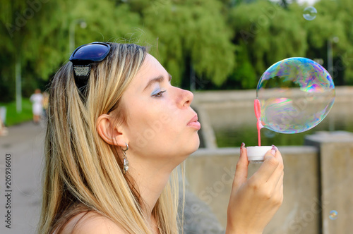 Attractive young woman enjoying in the park blowing soap bubbles