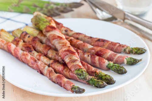 Healthy appetizer, green asparagus wrapped with bacon on white plate, horizontal