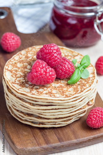 Stack of pancakes or fritters with raspberry on wooden board, raspberry jam on background, vertical