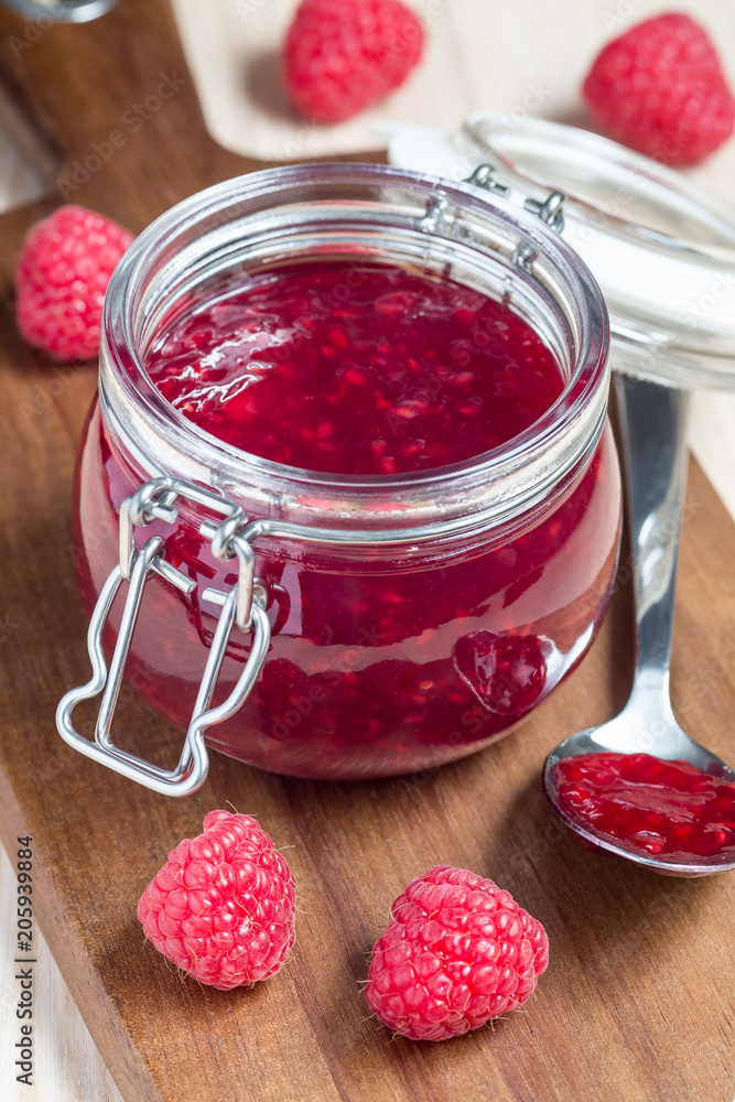Raspberry jam in glass jar on a wooden board, vertical