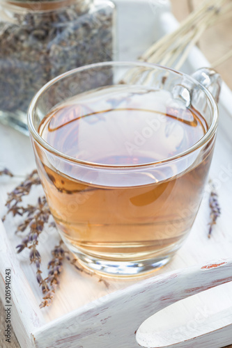 Herbal lavender tea in glass cup with lavender flowers on a wooden tray, vertical