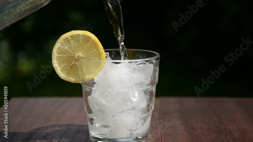 Pouring water with ice and lemon in glass, slow motion 