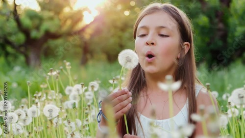 Cute girl blow on a dandelion at sunset. Rest at nature. Slow motion