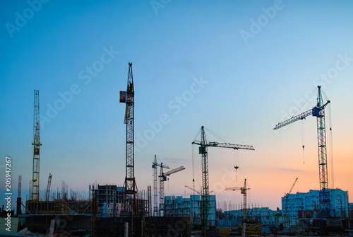 Industrial landscape with silhouettes of constraction cranes on dramatic sunset background