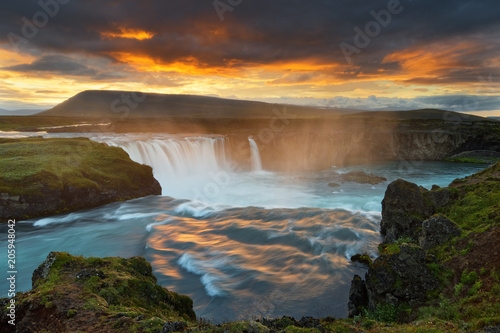 Scenic view of a waterfall in a wide sunset landscape, the colorful light reflected in the water, dark clouds above the scene - Location: Iceland, Godafoss (Goðafoss)