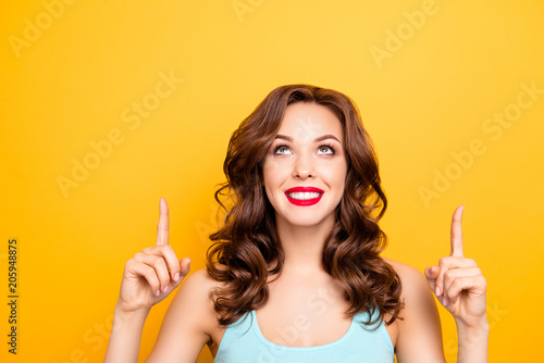 Portrait of pretty trendy girl with modern hairdo pointing two forefingers up showing copy space empty place isolated on yellow background, advertisement concept
