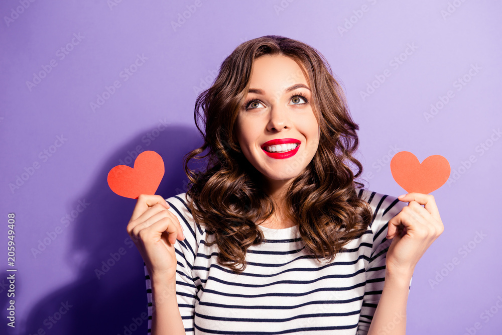 Portrait of thoughtful ponder girl in good mood having two little small red paper carton hearts in hands looking up isolated on violet background Portrait of thoughtful ponder girl in good mood having two little small red paper carton hearts in hands looking up isolated on violet background