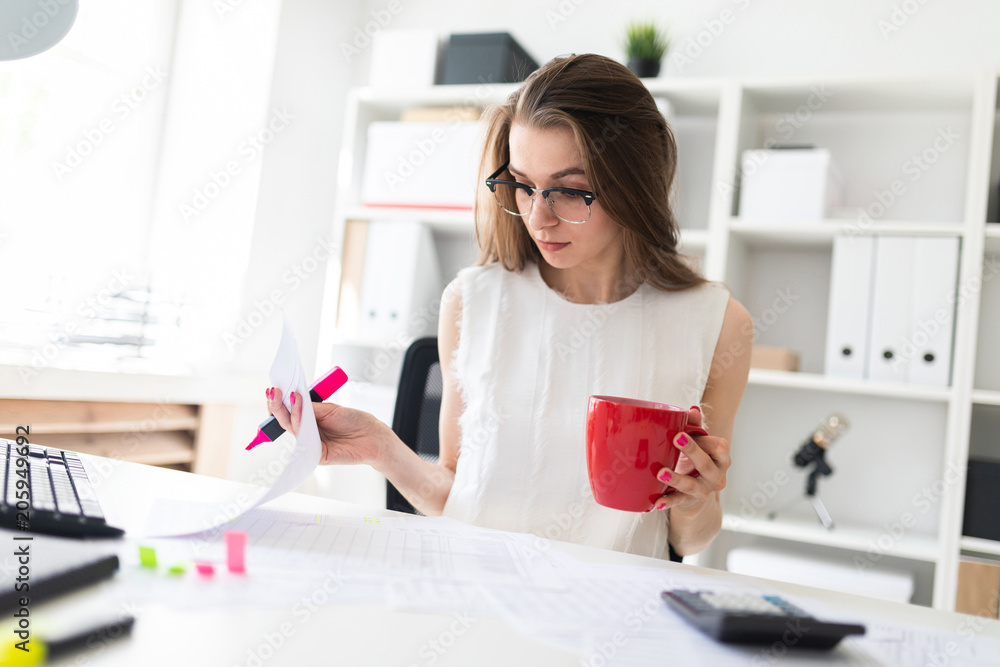 A young girl in the office holds a pink marker, a red mug and works with documents. A young girl in the office holds a pink marker, a red mug and works with documents.