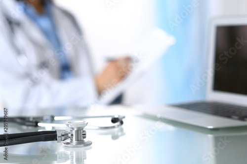 Stethoscope lying on glass desk with laptop computer at busy physician background. Medicine or pharmacy concept. Medical tools at doctor working table