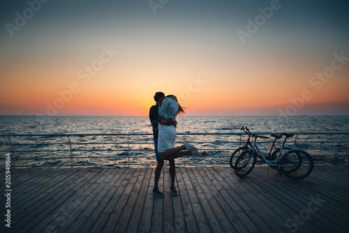 Couple of young hipster lovers kissing at the beach at sunrise sky at wooden deck summer time © Iryna Budanova