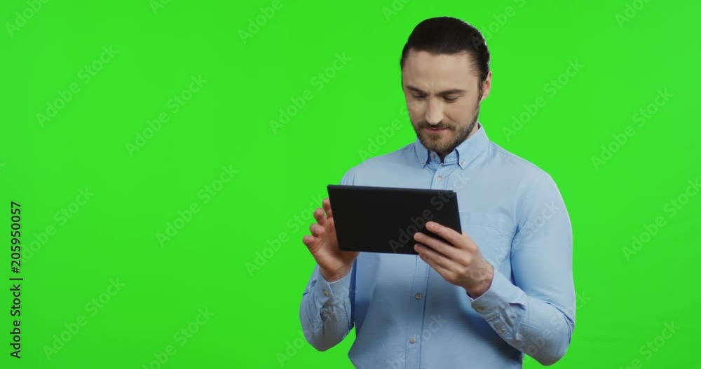 Portrait shot of the young attractive Caucasian businessman in the blue shirt scrolling and taping on the tablet, then doing yes gesture on the chroma key background. Green screen. Portrait shot of the young attractive Caucasian businessman in the blue shirt scrolling and taping on the tablet, then doing yes gesture on the chroma key background. Green screen.