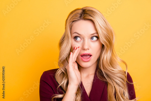 Portrait of concentrated big-eyed woman in classic outfit hiding mouth with palm whispering gossips, telling secret looking to the side with eyes isolated on yellow background
