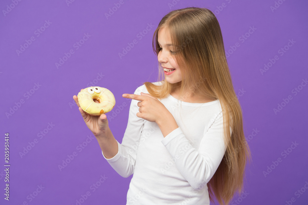 Happy kid point finger at donut on violet background. Little girl with glazed ring doughnut on purple backdrop. Unhealthy eating. Child smile with junk food. Food and dessert. Childhood and childcare Happy kid point finger at donut on violet background. Little girl with glazed ring doughnut on purple backdrop. Unhealthy eating. Child smile with junk food. Food and dessert. Childhood and childcare