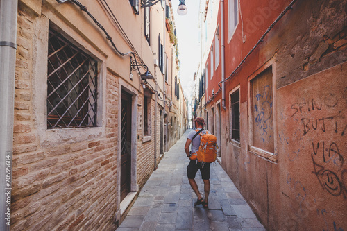 tourist with an orange backpack and bandana walks along narrow street in Europe. Italy Venice in summer. The facade of old houses without people and crowds of tourists. Unpublished places in Venice. © Elizaveta