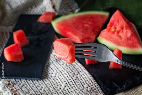 Closeup of a composition of fresh fruit of the summer, watermelon on white background with slate. Mediterranean diet with varied summer fruits. Stock photo. Top front view. Hand with fork pricking 
