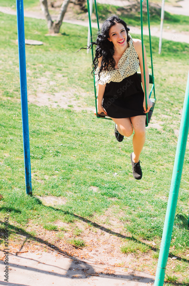 Beautiful Girl, brunette with red lips. Spring , shooting in the Park . Wearing a dress and high heel shoes, kataetsya at kachele