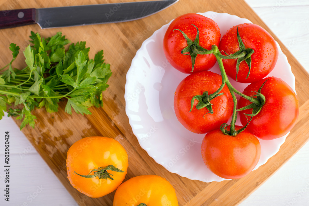 Fresh red and yellow tomatoes from above on a wooden board with a knife in a white plate at a white textured table Fresh red and yellow tomatoes from above on a wooden board with a knife in a white plate at a white textured table