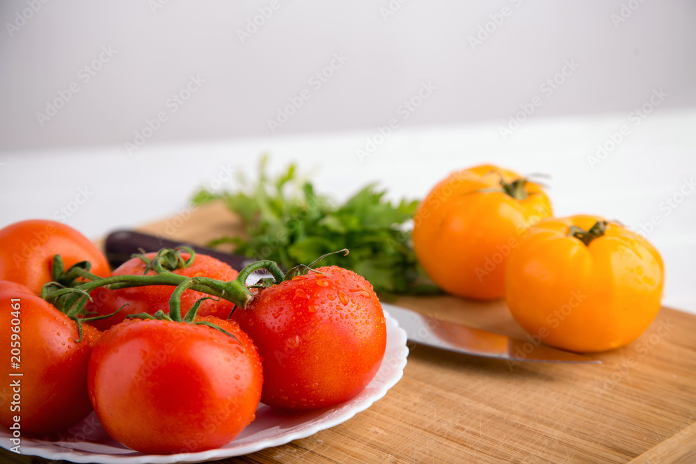 Fresh red and yellow tomatoes close up on a wooden board with a knife at a white textured table Fresh red and yellow tomatoes close up on a wooden board with a knife at a white textured table