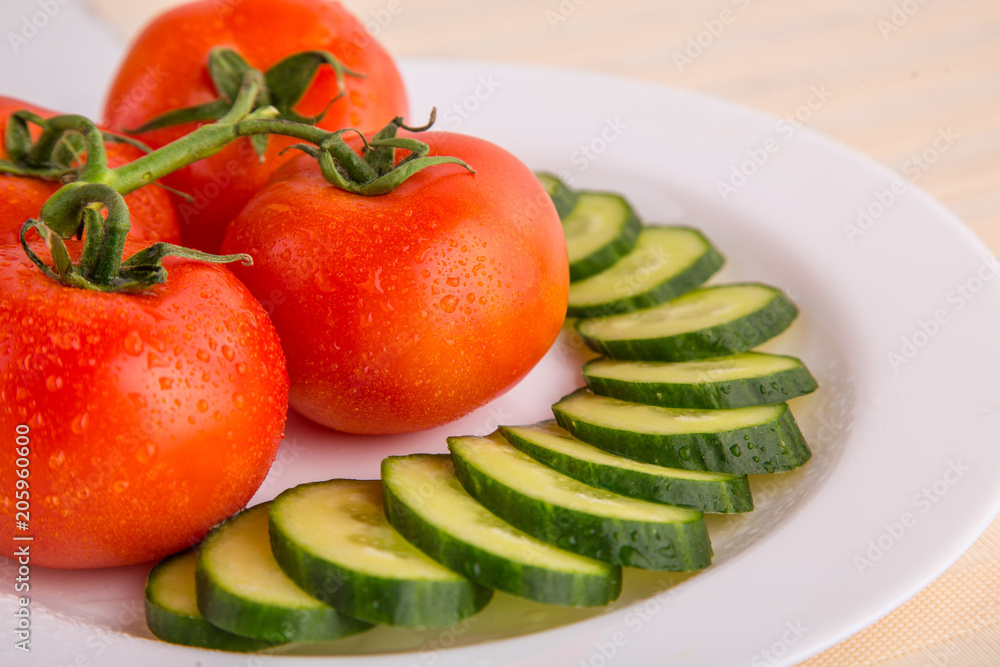 Fresh red tomatoes with sliced cucumber on a white plate close up