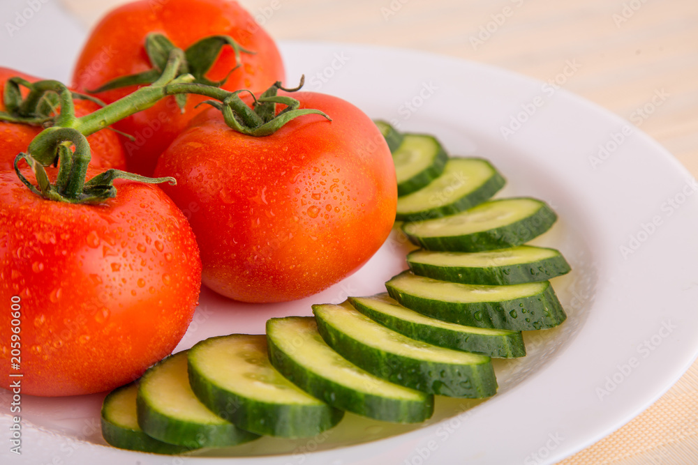 Fresh red tomatoes with sliced cucumber on a white plate close up Fresh red tomatoes with sliced cucumber on a white plate close up