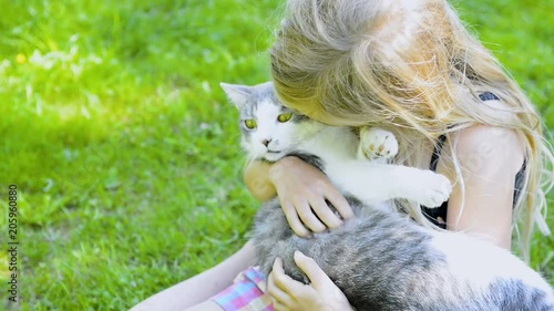  Cute little child blond girl with cat, girl playing with cat on the green grass lawn in the summer garden 

