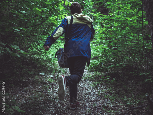 Canvas-taulu young scary man running away in the dark forest on the path back view