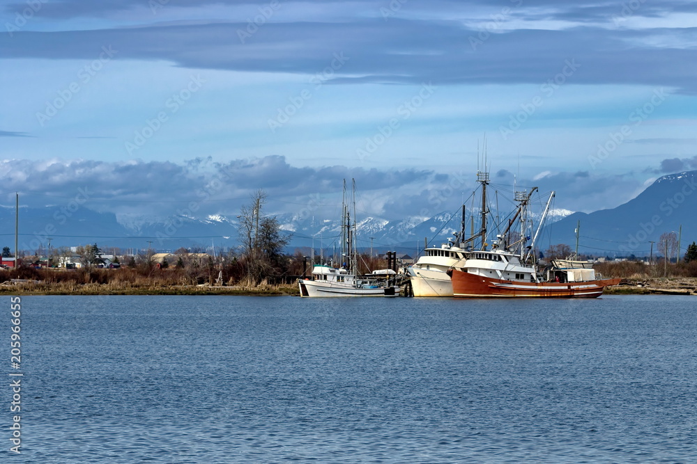 Fishing boats at the Marina near the village at the background of mountain range and cloudy sky