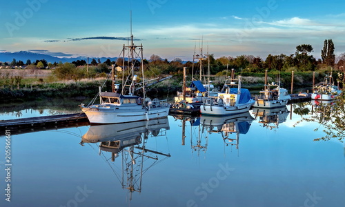 Beautiful reflection at the everning time of the Fishing boats at the marina near the village, at the background of mountain range and cloudy sky