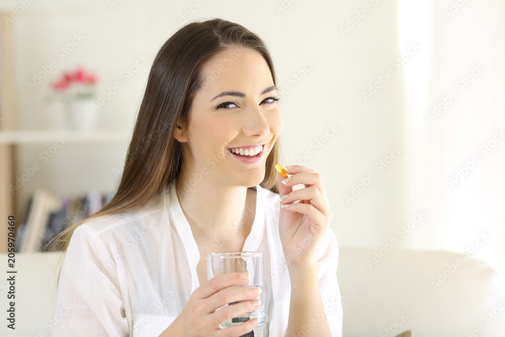 Happy woman taking a vitamin supplement pill looking at you Happy woman taking a vitamin supplement pill looking at you