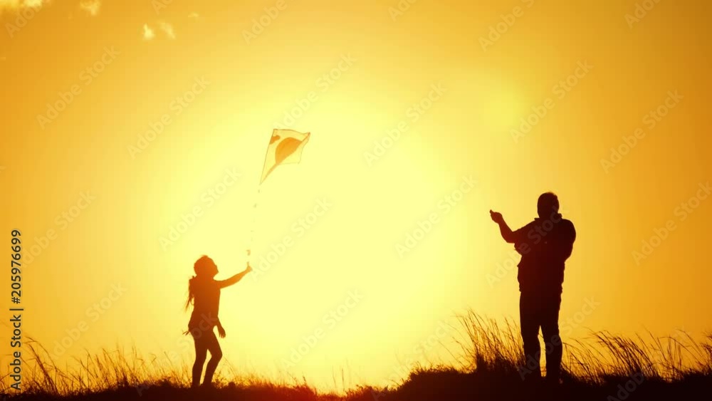 Silhouette of a happy family playing a kite. Grandpa and little girl are playing at sunset with a kite. Silhouette of a happy family playing a kite. Grandpa and little girl are playing at sunset with a kite.