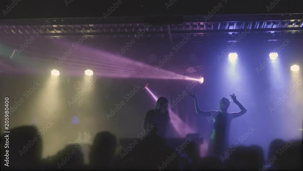 Two beautiful young women DJ play the music on the mixing console in the nightclub. Against the background of unrecognizable people. Slow motion Two beautiful young women DJ play the music on the mixing console in the nightclub. Against the background of unrecognizable people. Slow motion