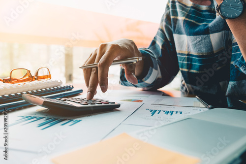 Close up of businessman or accountant hand holding pen working on calculator to calculate business data, accountancy document and laptop computer at office, business concept photo