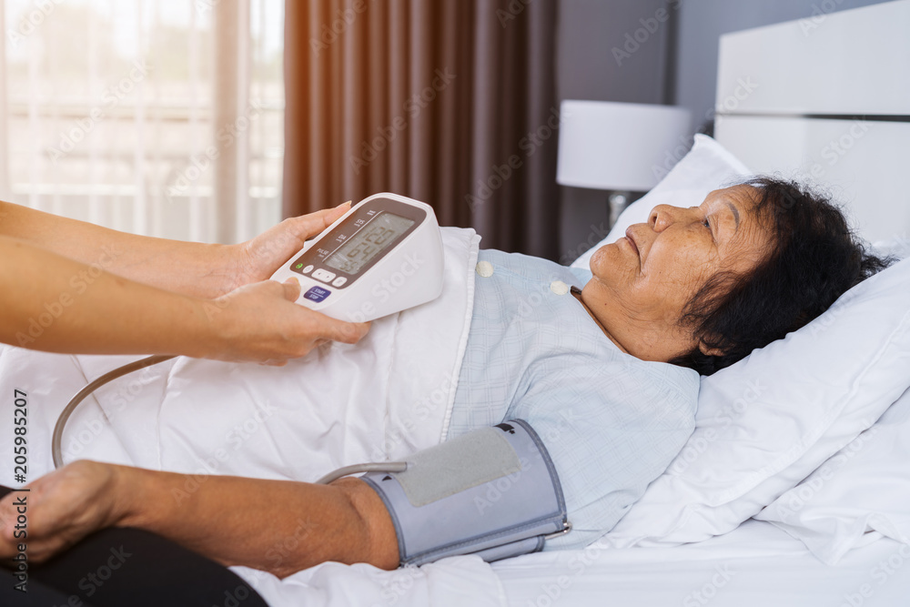 nurse checking blood pressure of a senior woman on bed nurse checking blood pressure of a senior woman on bed