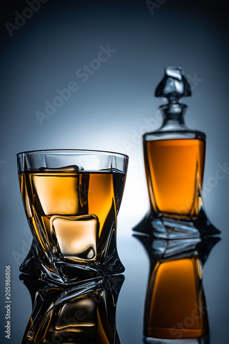 selective focus of whiskey glass with ice cubes and bottle, on grey