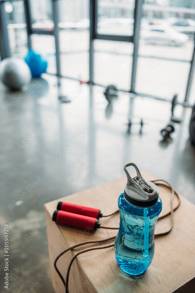 Naklejka premium closeup view of jump rope and bottle of water on wooden box at gym