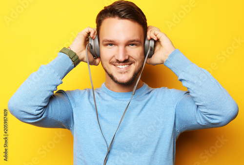 lifestyle and people concept: Happy young man listening to music with headphones over yellow background