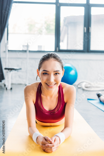 smiling asian sportswoman in wristbands on fitness mat at gym Free Download smiling asian sportswoman in wristbands on fitness mat at gym - GFXLoad