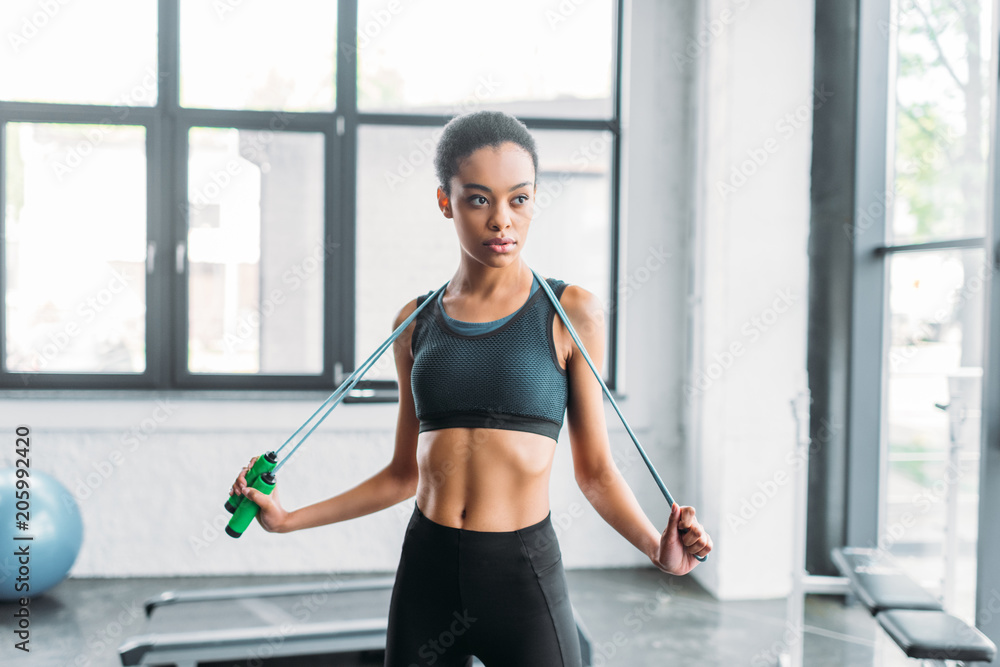 portrait of young african american sportswoman with jumping rope at gym