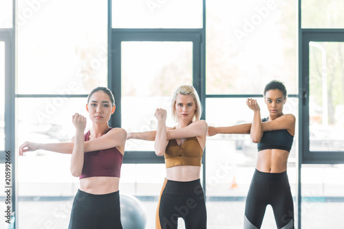 portrait of attractive multiracial sportswomen stretching before working out at gym