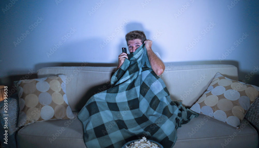 lifestyle portrait of attractive scared and nervous man watching suspense  horror movie on television feeling stressed covering with blanket in panic  Stock Photo | Adobe Stock