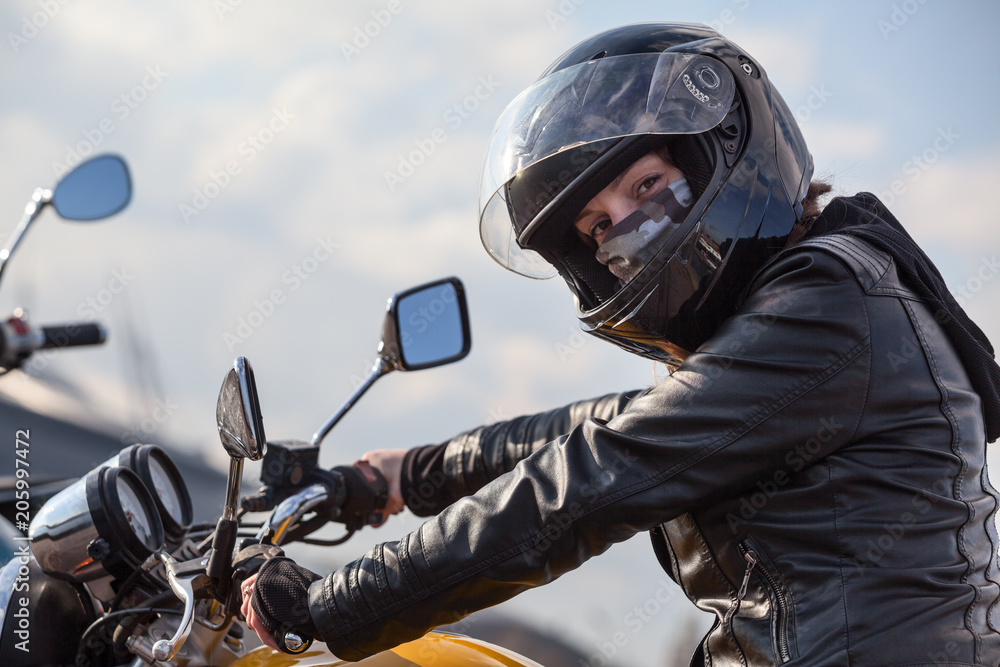 Naklejka premium Kierowca motocykla w czarnym stroju trzymając kierownicę i patrząc na kamery, Kaukaski kobieta