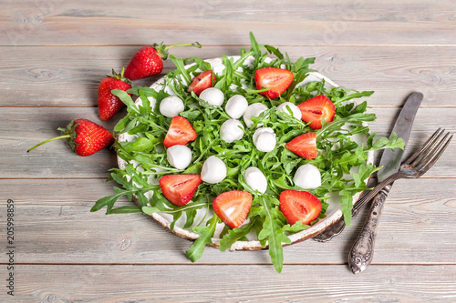 Delicious rucola salad with mozzarella and strawberries on a wooden background. Healthy foods photo