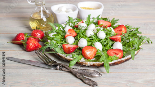 Delicious rucola salad with mozzarella, strawberries, olive oil and spices on a wooden background. Healthy foods. Banner photo