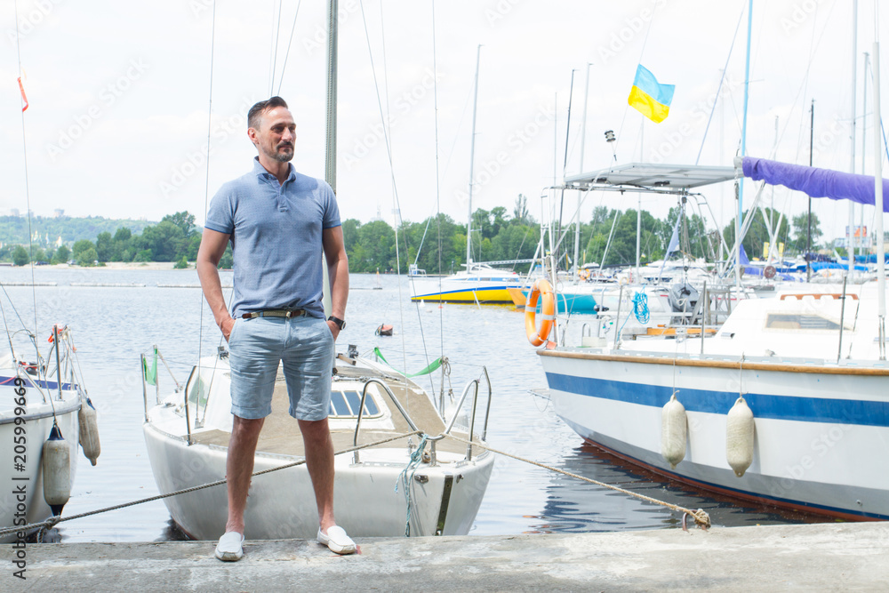 Obraz premium Attractive man stands at the nose of a boats on pier at river marina