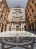 Female tourist standing in the courtyard of the Benedictine monastery of Santa Maria de Montserrat with hands raised, near Barcelona, Spain