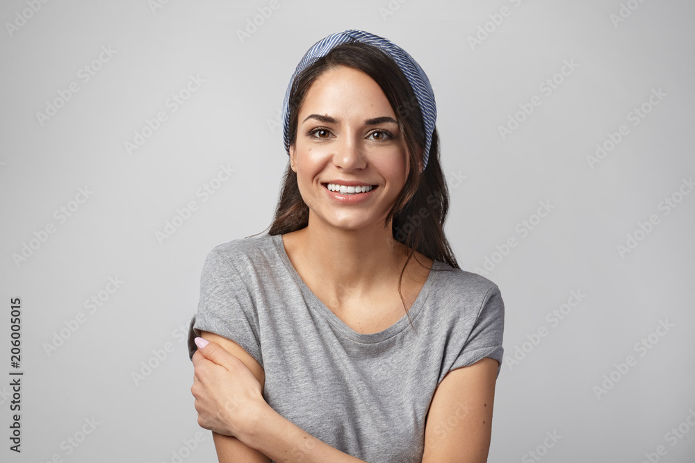 Portrait of happy beautiful young housewife wearing casual gray t-shirt and head band smile joyfully at camera, feeling glad that she finished all housework and now going to watch favorite series Portrait of happy beautiful young housewife wearing casual gray t-shirt and head band smile joyfully at camera, feeling glad that she finished all housework and now going to watch favorite series