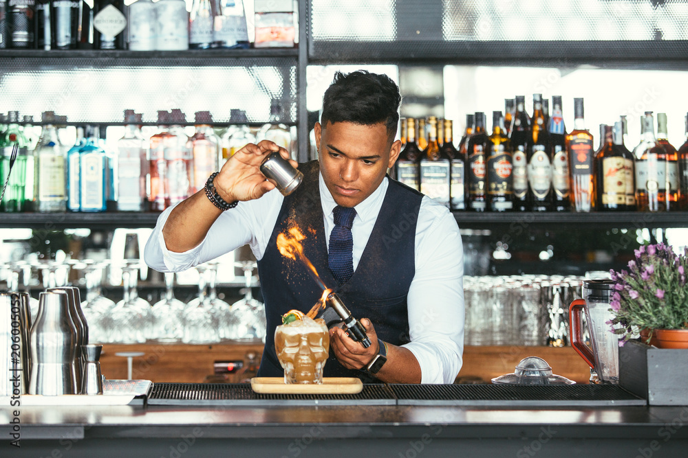 Concentrated expert bartender uses a blowtorch for a cocktail
