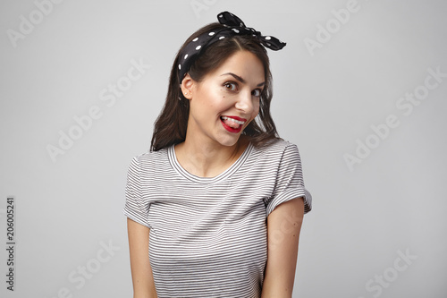 Picture of sassy beautiful young Caucasian brunette woman wearing bright make up sticking out tongue playfully, smiling at camera, having childish or coquettish look, feeling upbeat and excited