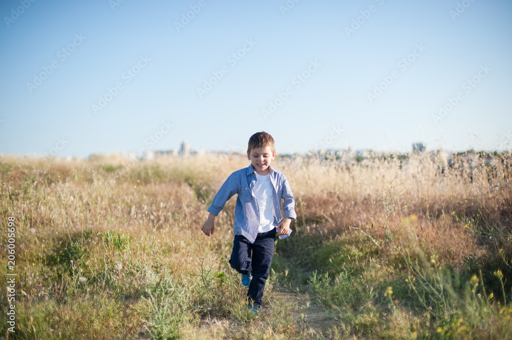 happy smiling little kid walking among yellow grass in summer sunny day