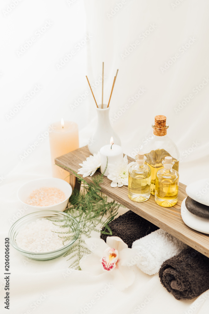 close up view of arrangement of spa treatment accessories with towels, oil and salt on white background